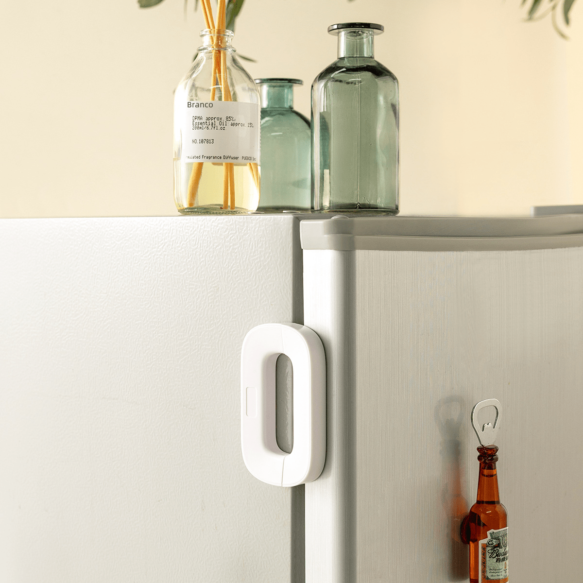 White refrigerator handle on a white refrigerator with bottles and a plant in the background.
