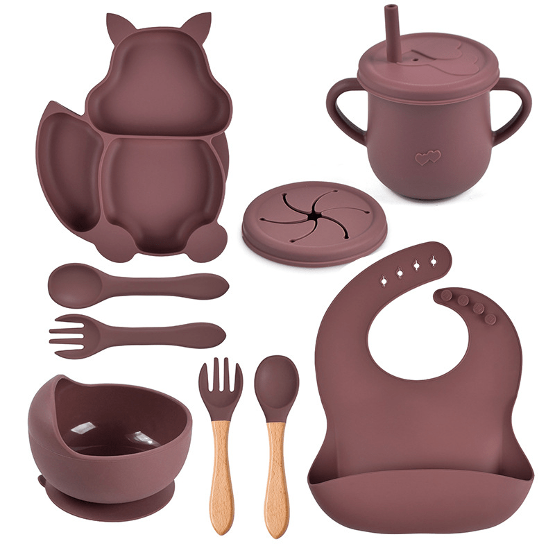 Children's silicone dining set with various pieces including a cup, bowl, spoon, and bib on a white background.