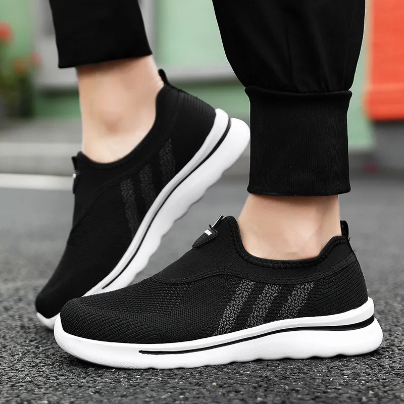 Black athletic shoes with white soles worn by a person on a road.