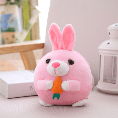 Pink plush toy with bunny ears and a carrot on a light surface.