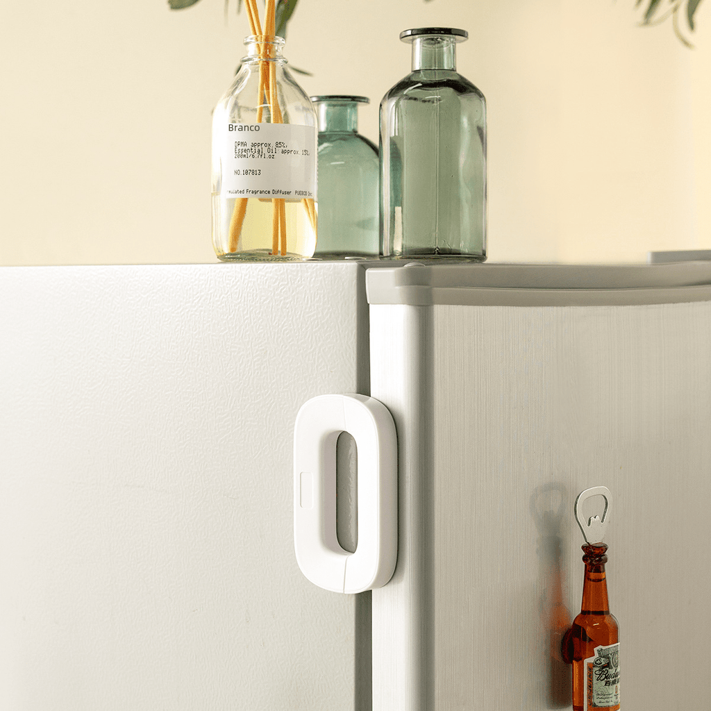 White refrigerator handle on a white refrigerator with bottles and a plant in the background.