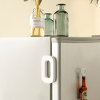 White refrigerator handle on a white refrigerator with bottles and a plant in the background.