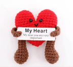 Crocheted heart-shaped character holding a sign with a message on a white background