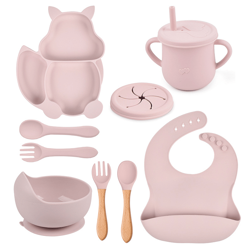 Pink baby feeding set including bowl, cup, spoon, and bib on a white background