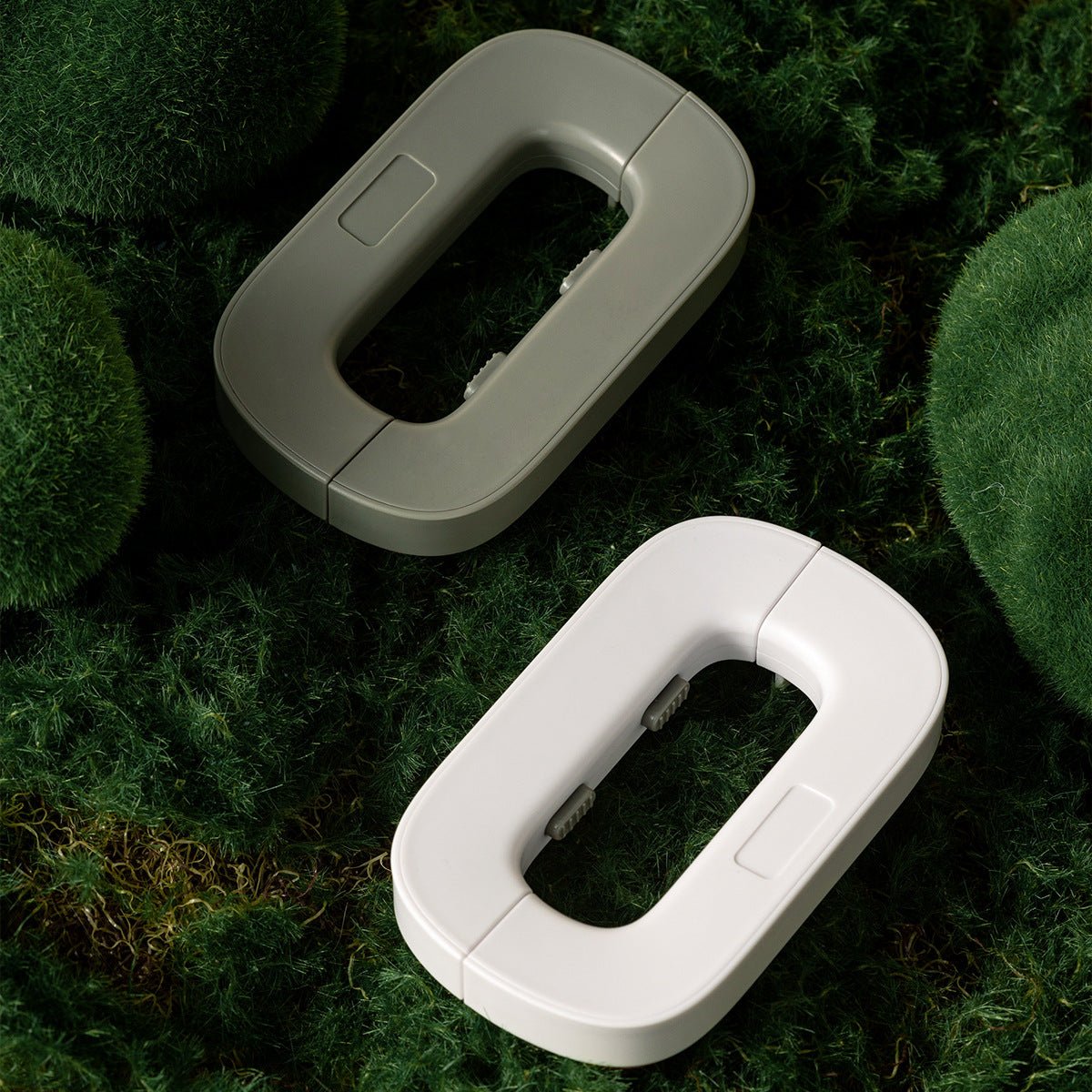 Two oval-shaped devices, one gray and one white, on a grassy background.